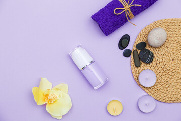 Scented candles, towel, lotion and pebbles on a lilac background.