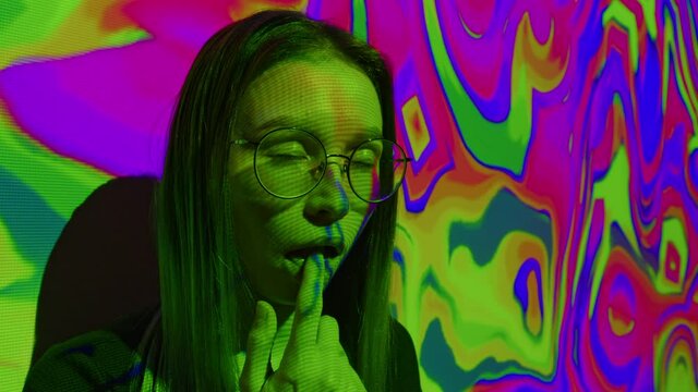 A young woman puts a lsd acid blotter on her tongue. Multicolored psychedelic abstract background. The concept of psychedelia, nirvana and addiction