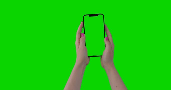 Woman hands holding the smartphone on green screen chroma key background. Mock-up for your product. The newest iPhone 12 Pro Max model in vertical orientation portrait mode.