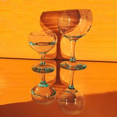 A glass of pure fresh water.  Glass with strong shadows. Orange background.Reflected in mirror.Refraction of light by a glass.