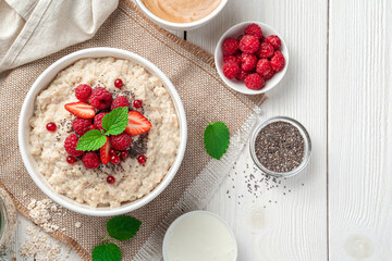 Oatmeal porridge with fresh berries, chia seeds and mint on a light background. Top view, copy space.