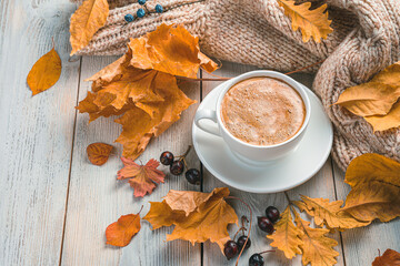 A cup of coffee, autumn foliage and a cozy sweater on a beige background. Autumn morning.
