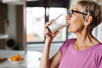Profile view of a woman drinking fresh milk from a glass in the kitchen