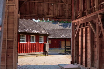 Fototapeta na wymiar Red wooden outbuildings on a farm visible through one of the open doors of a barn.