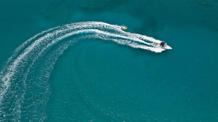 Aerial drone photo of woman practicing high speed water ski towed by large speed boat in emerald...