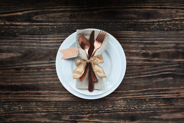 A holiday place setting with plate, napkin, silverware and blank tag for Thanksgiving Day or Christmas over a rustic table shot from flat lay or top view position. 