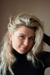 A beautiful blonde girl with long hair looks at the camera and holds her hair with her hand. Photographed from the front