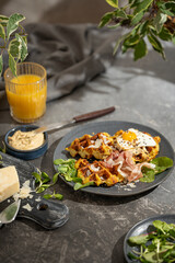 Savory vegetable waffles with cheese, egg, orange juice on grey textured table - beautiful healthy diet breakfast. Farm country concept. Copy space. Homemade pastry. Sunny light.