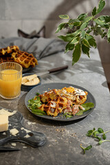 Savory vegetable waffles with cheese, egg, orange juice on grey textured table - beautiful healthy diet breakfast. Farm country concept. Copy space. Homemade pastry. Sunny light.