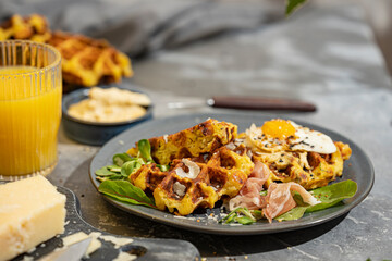 Savory vegetable waffles with cheese, egg, orange juice on grey textured table - beautiful healthy diet breakfast. Farm country concept. Copy space. Homemade pastry. Sunny light.