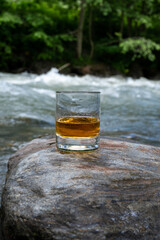 Glass of strong scotch single malt whisky with fast flowing mountain river on background