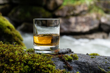 Glass of strong scotch single malt whisky with fast flowing mountain river on background