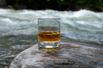 Glass of strong scotch single malt whisky with fast flowing mountain river on background