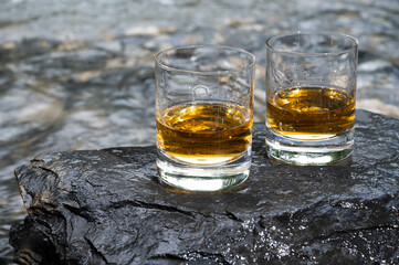 Glass of strong scotch single malt whisky with fast flowing mountain river on background