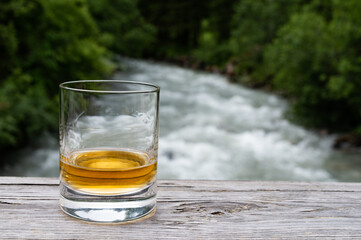 Glass of strong scotch single malt whisky with fast flowing mountain river on background
