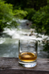 Glass of strong scotch single malt whisky with fast flowing mountain river on background