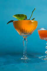 mandarin tangerine in cocktail drink glass splash blue background
