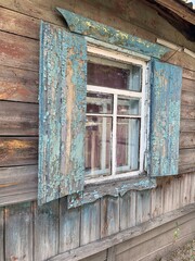 An old wooden window with green shutters on an old wall with cracked blue paint.
