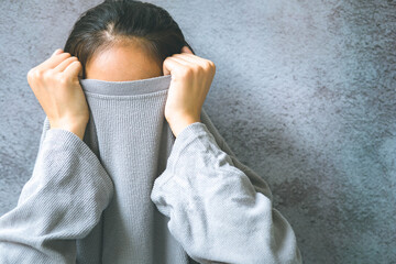 Asian woman hiding face under the clothes. She is oulling sweater on her head. She has social...
