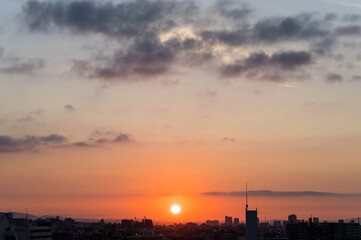 Fototapeta na wymiar 兵庫県神戸市東灘区のマンション高層階から撮影した日の出。梅雨明け後、まだ雲が残るが、オレンジ色に染まりドラマチックな都会の朝。