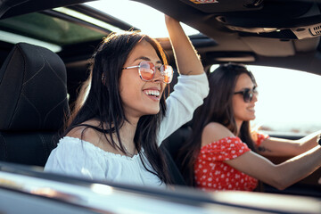 Pretty young women singing while driving a car on road trip on beautiful summer day.