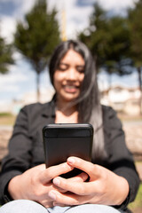 detail of latina woman's hands using a cell phone with out-of-focus background