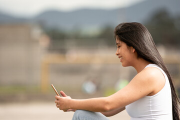 Young latina girl with long hair using a cell phone with the background out of focus.