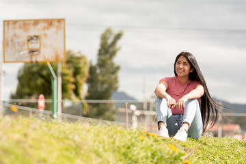 Fototapeta premium smiling Hispanic girl sitting in a green area, relaxation concept
