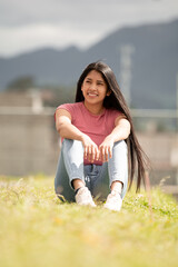 smiling hispanic girl sitting in a green area, concept of freedom