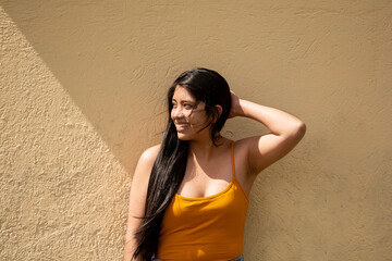 young happy latin woman leaning against a yellow wall, concept of happiness