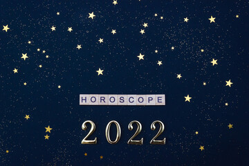 Word Horoscope and numbers 2022. Wooden blocks with lettering on blue background decorated with golden stars confetti. Flat lay, top view