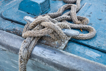 Old, wet rope wrapped around a metal cleat on a blue boat.