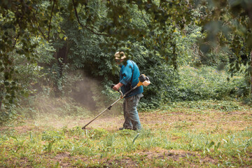 a worker mows the grass with a trimmer