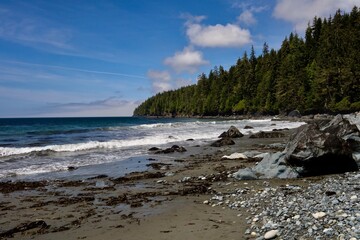 Fototapeta na wymiar Mystic Beach shoreline with blue sky, trees, rocks and surf. Iconic scene from the west coast of Vancouver Island, British Columbia, Canada. 