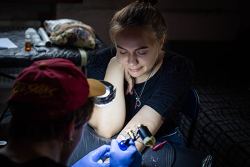 cropped shot of tattooing process on hand in salon. A professional tattoo artist introduces ink into the skin using a needle from a tattoo machine.Professional tattooist working in studio.
