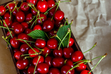 Close-up cropped box, crape of dark red sweet cherries with tail on craft wrinkled paper background. Summer fruits and berries. Harvest and crop concept. Organic food. Top view. Summertime