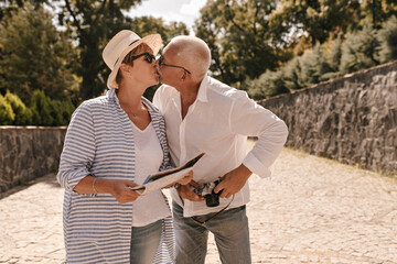 Beautiful woman with shirt blonde hair in hat and long striped blouse kissing with grey haired man...