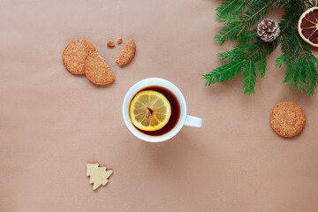 Fototapeta na wymiar Christmas tree branches, cup of tea with lemon and cookies on beige background. Top view, flat lay, copy space