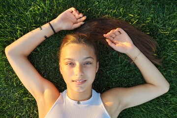 Portrait of a teenage girl, top view, smiling beautiful female lying on green grass