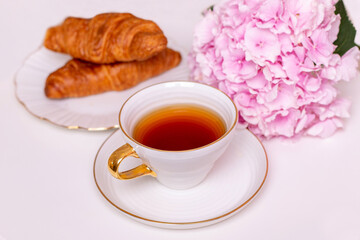 Cup of tea and croissants with hydrangea flower on white background