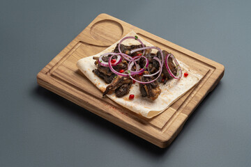 shashlik or grilled meat with onion on pita on wooden board on grey background