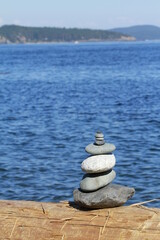 Rock stacking on a log with the blue ocean in behind. 