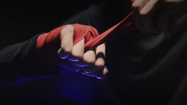 Male boxer wrapping hands before fighting in slow motion. Close-up of young athlete getting ready for fight. Man preparing. Sport concept. Close up boxer wrapping red bandages
