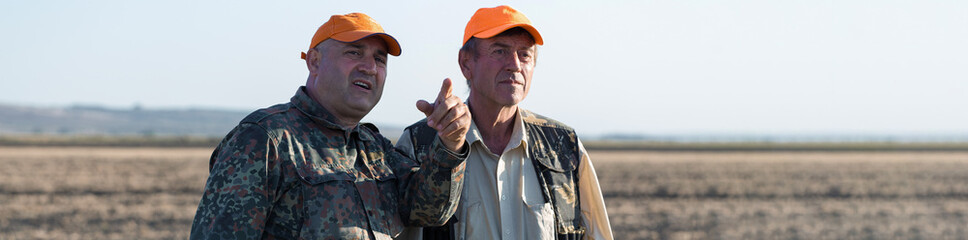 Duck hunters with shotgun walking through a meadow.