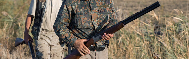 Duck hunters with shotgun walking through a meadow.