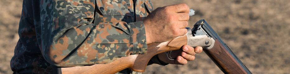Duck hunter with shotgun walking through a meadow.