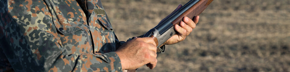 Duck hunter with shotgun walking through a meadow.