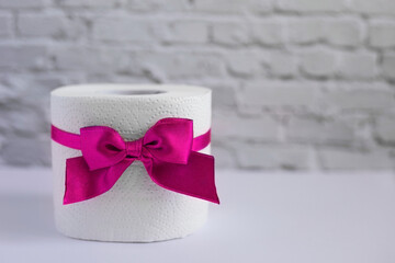 Roll of white toilet paper tied with pink ribbon with a bow. Toilet roll with magenta bow