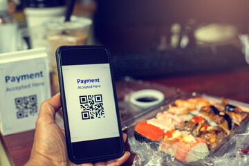 Obraz na płótnie Canvas Customer hand using smart phone to scan QR code tag with blur Sushi set or Japanese food meal on desk to accepted generate digital pay without money for food delivery payment. Qr code payment concept