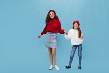 Charming lady in red oversize shirt and denim skirt holding har her ginger sister in hat, white...